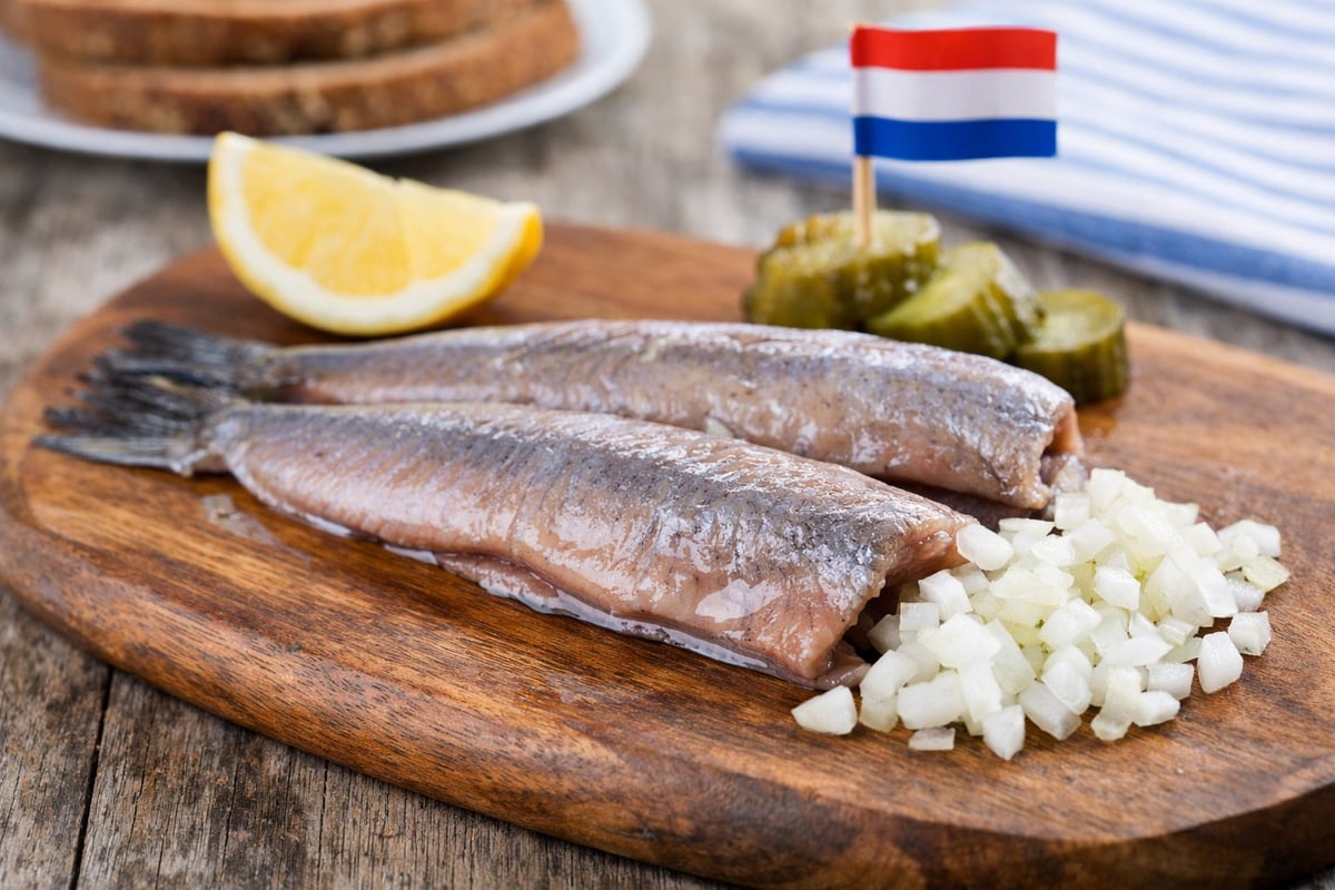 Hollandse haring op een houten plank met uitjes, augurk, citroen en een Nederlandse vlag